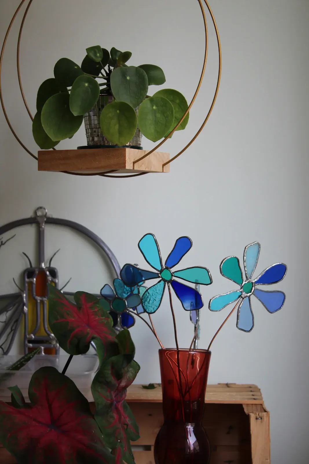 Fleurs stylisées en vitrail bleu sur tige de cuivre disposées dans un vase rouge à l'intérieur.