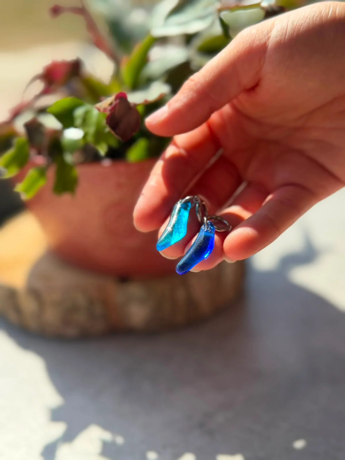 Boucles d'oreilles en verre bleu translucide tenues dans la main devant une plante.