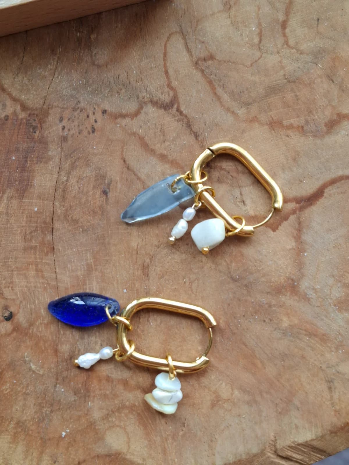 Paire de boucles d'oreilles dorées à breloques en verre bleu et perles blanches posées sur du bois.