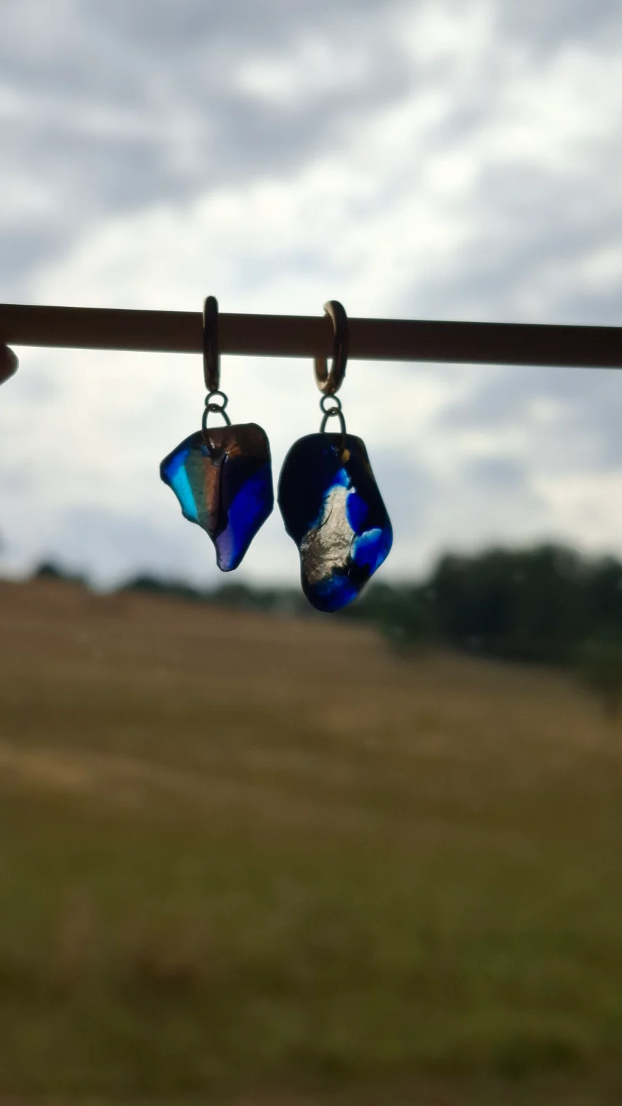 Boucles d'oreilles en verre bleu et translucide suspendues en extérieur face au ciel.