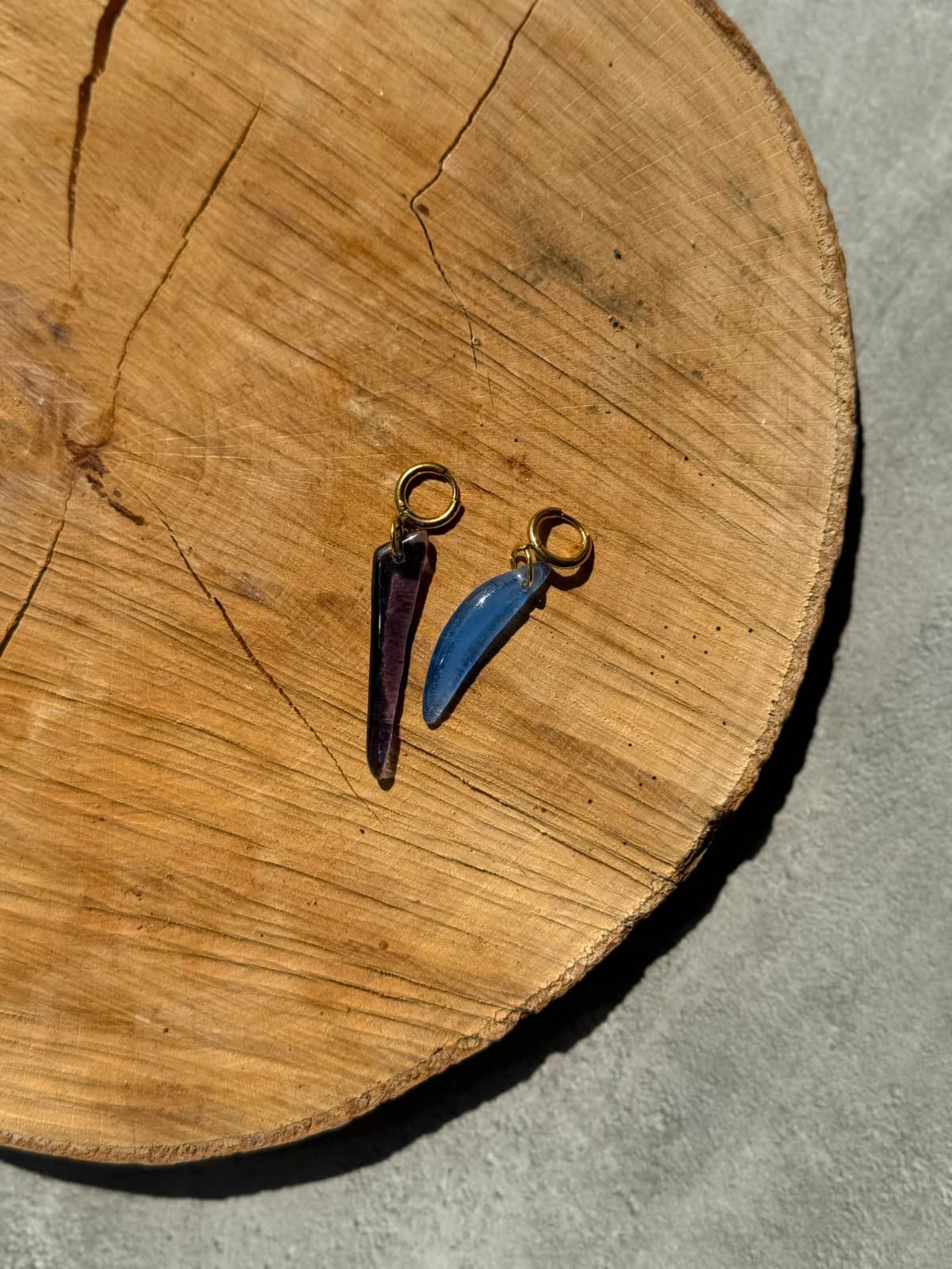 Paire de boucles d'oreilles pendantes en verre bleu et violet posées sur une tranche de bois.