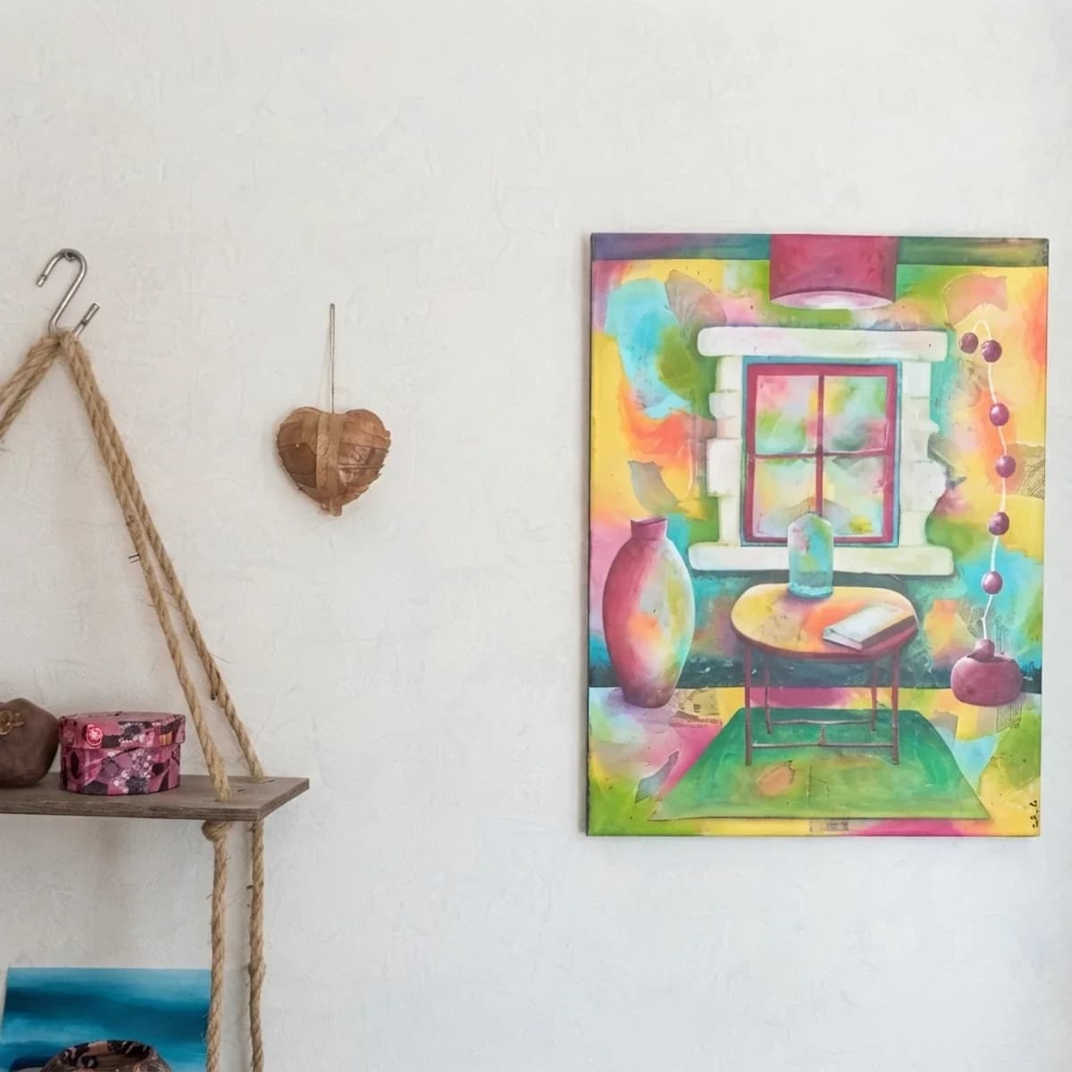 Tableau d'intérieur coloré accroché sur un mur blanc à côté d'une étagère suspendue.