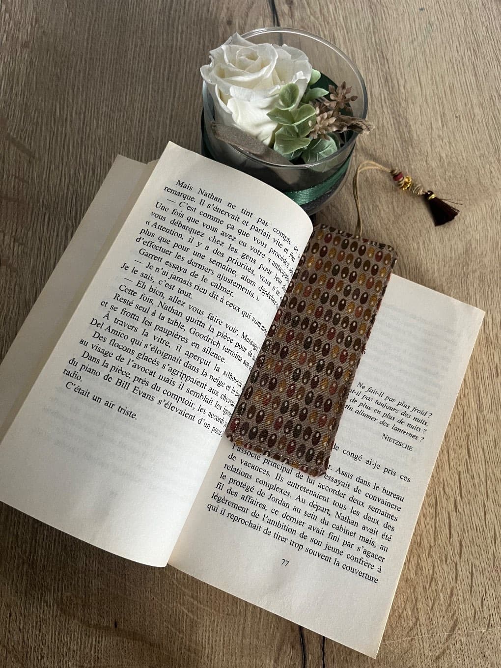 Marque-page en tissu à motifs marron et ocre avec cordon à pompon et perles sur table en bois.