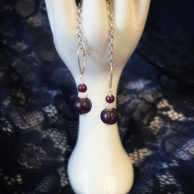 Boucles d'oreilles pendantes présentées sur une main porte-bijoux blanche devant une dentelle noire.