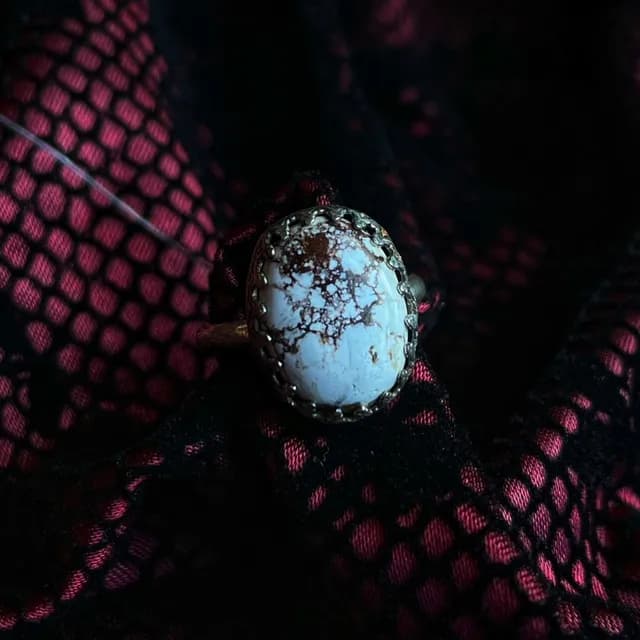 Gros plan sur le cabochon ovale blanc veiné de marron serti sur une monture argentée crantée.