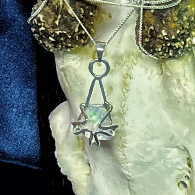 Gros plan du pendentif ajouré en argent mettant en valeur les reflets lumineux de l'opale