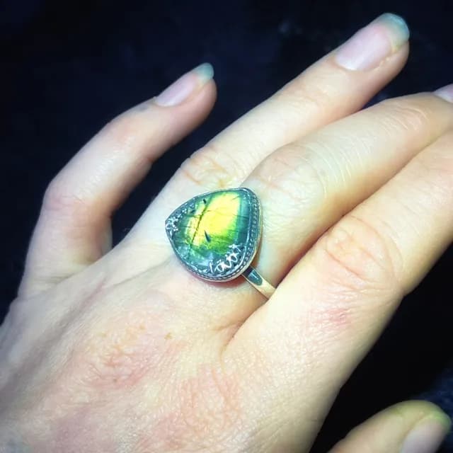 Bague en argent portée au doigt, sertie d'une labradorite triangulaire aux reflets verts et dorés