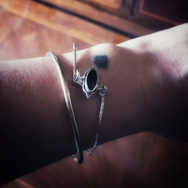 Gros plan sur le bracelet rigide en argent et sa pierre noire ovale au poignet.