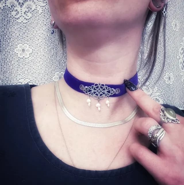 Ras de cou en velours violet avec pièce centrale filigranée et perles blanches pendantes au cou.