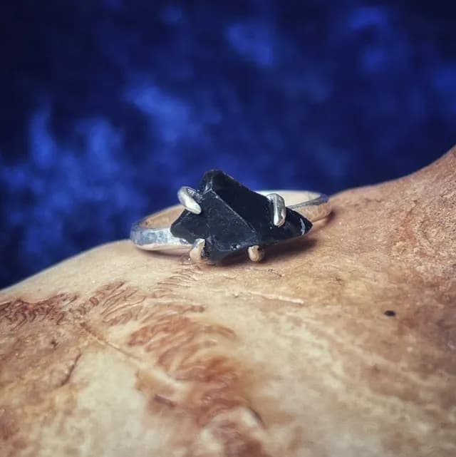 Gros plan sur la bague argentée sertie d'une pierre noire brute sur fond bleu texturé.