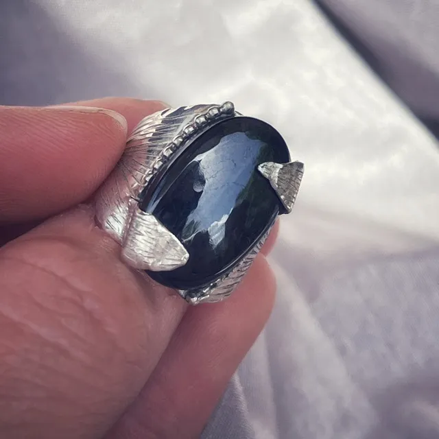 Bague en argent avec pierre purpurite sombre et griffes gravées en forme de pétales, tenue en main