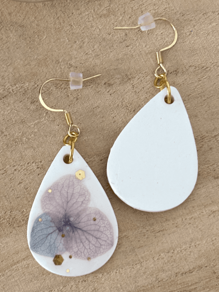 Gros plan sur la paire de boucles d'oreilles en résine blanche aux détails floraux mauves.