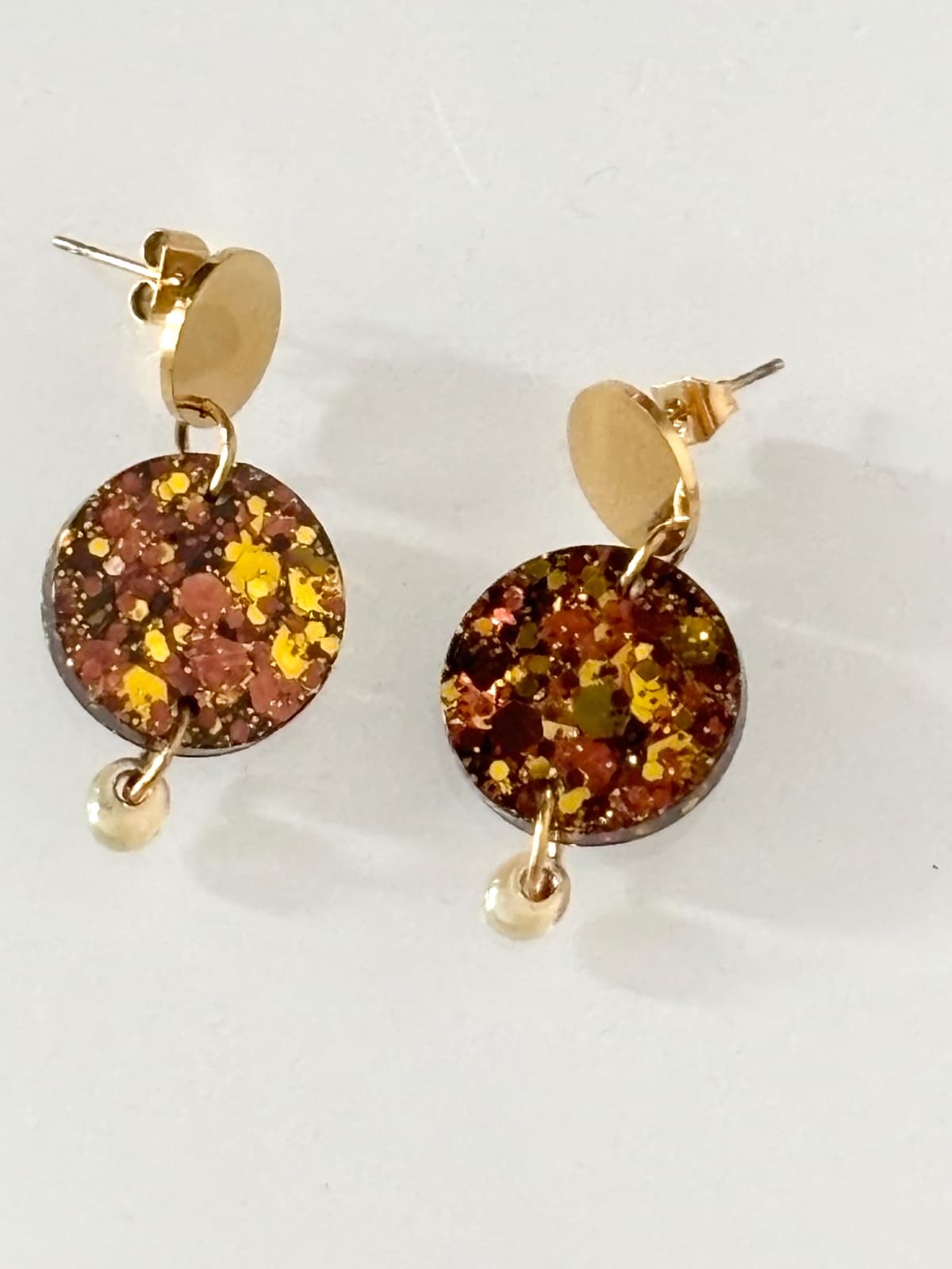 Paire de boucles d'oreilles dorées à médaillon pailleté et perle ambre sur fond blanc