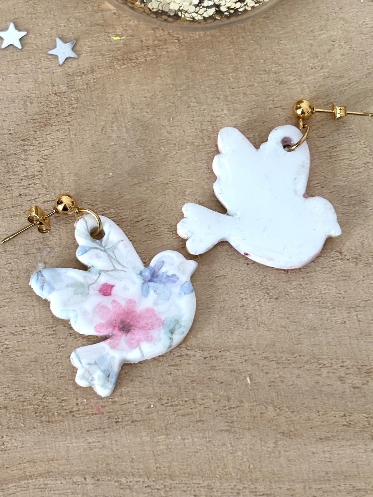 Face avant fleurie et dos blanc uni des boucles d'oreilles oiseau en pâte polymère sur bois.