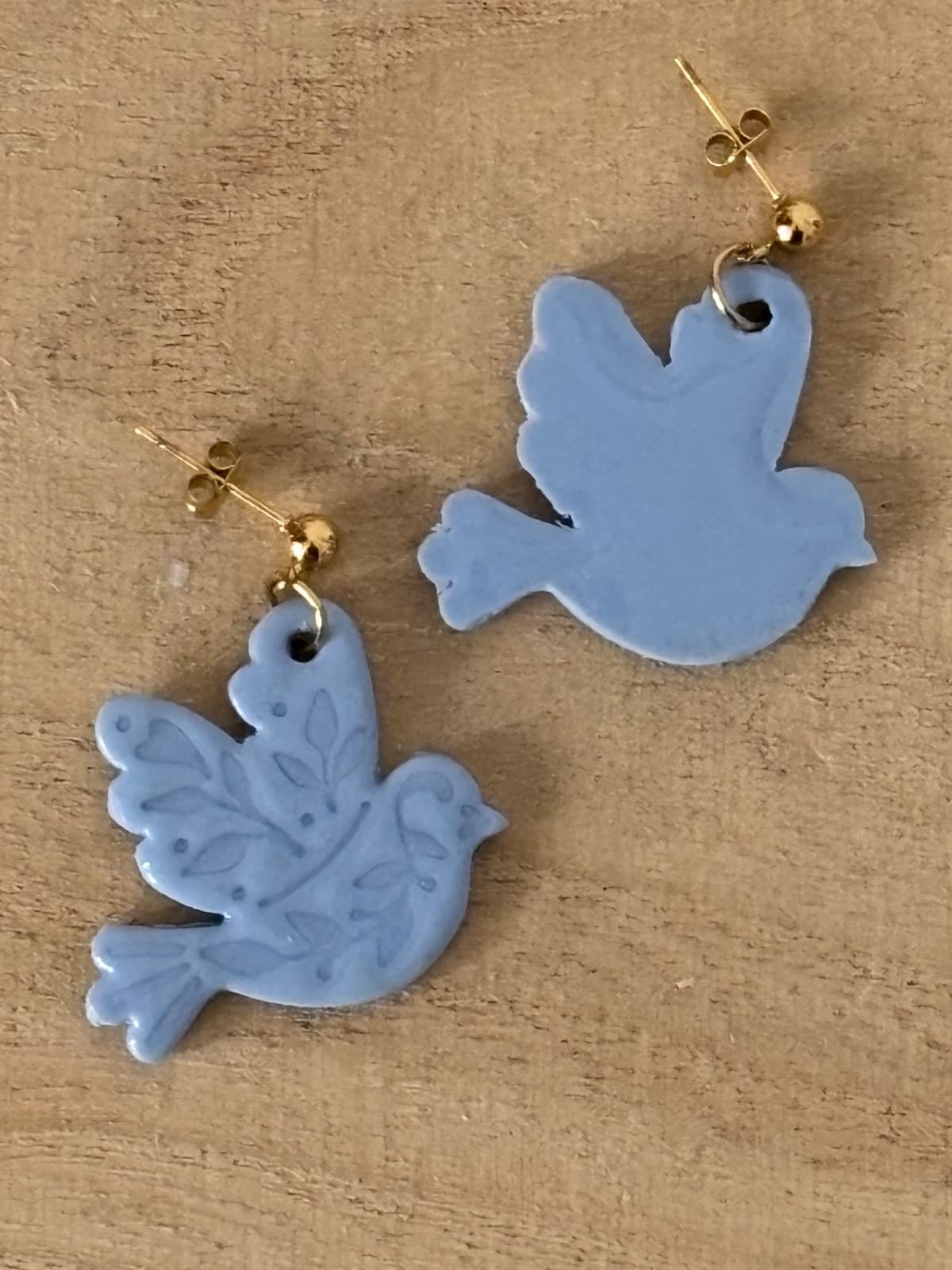Vues recto et verso des boucles d'oreilles oiseaux bleu gris posées sur une surface en bois