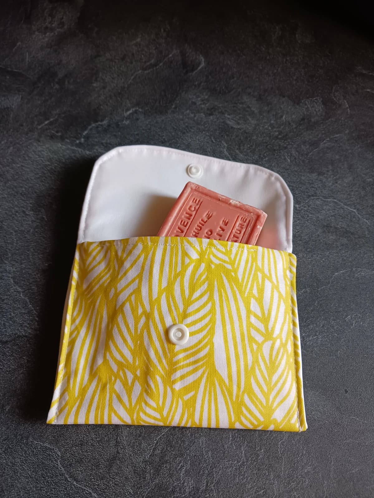 Pochette ouverte en tissu à motifs végétaux jaunes avec un savon à l'intérieur et doublure blanche