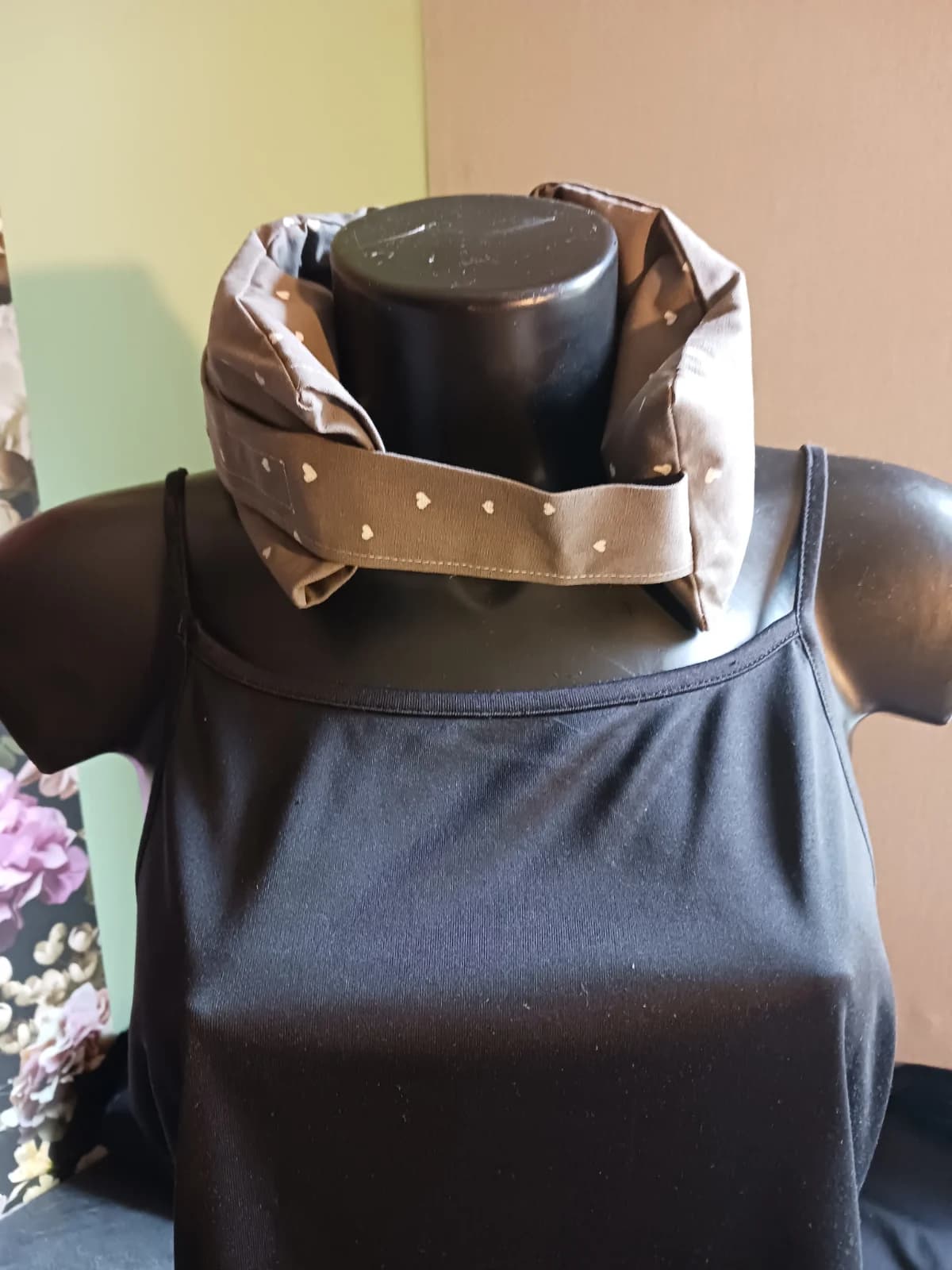 Bouillotte tour de cou taupe à motifs cœurs blancs, fermée sur le buste d'un mannequin.
