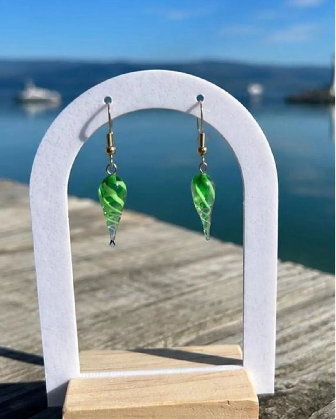 Paire de boucles d'oreilles coquillage vert en verre filé suspendue sur un présentoir devant la mer.