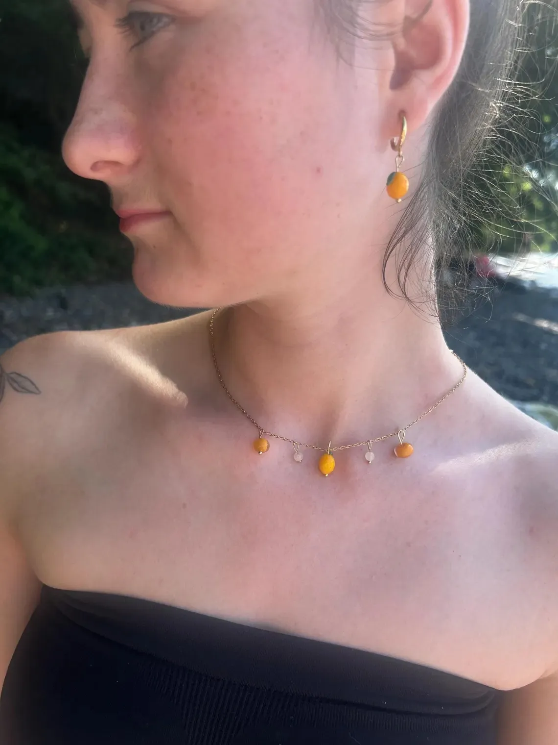 Boucles d'oreilles pendantes en verre en forme de citron jaune sur un présentoir arche posé sur des galets.