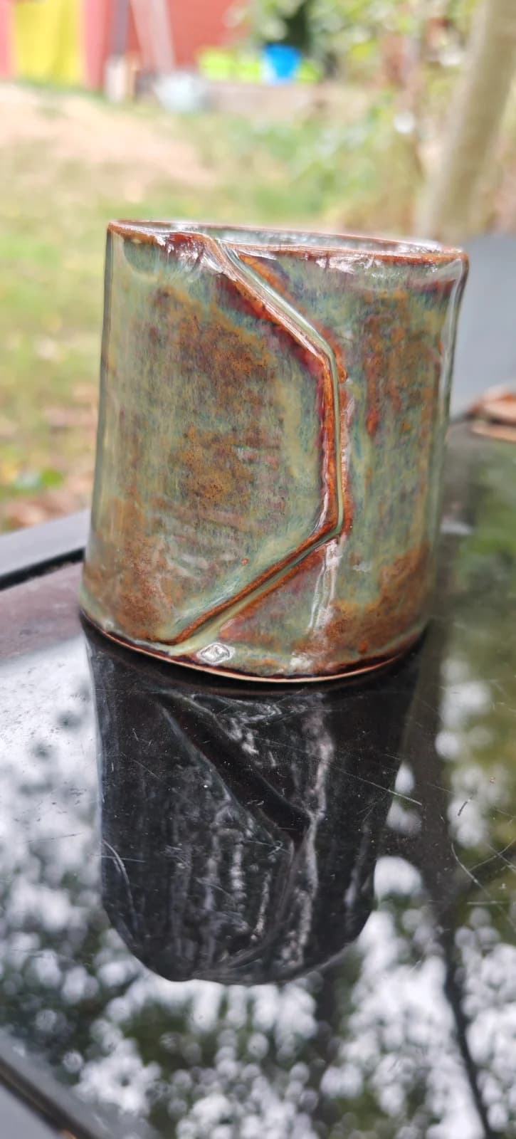 Gobelet en céramique émaillée vert et rouille avec pli en relief, posé sur une surface sombre