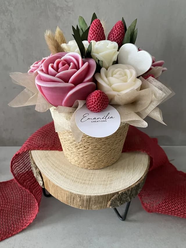 Bouquet décoratif de roses rose poudré et crème avec fausses fraises dans un pot tressé sur un socle en bois.