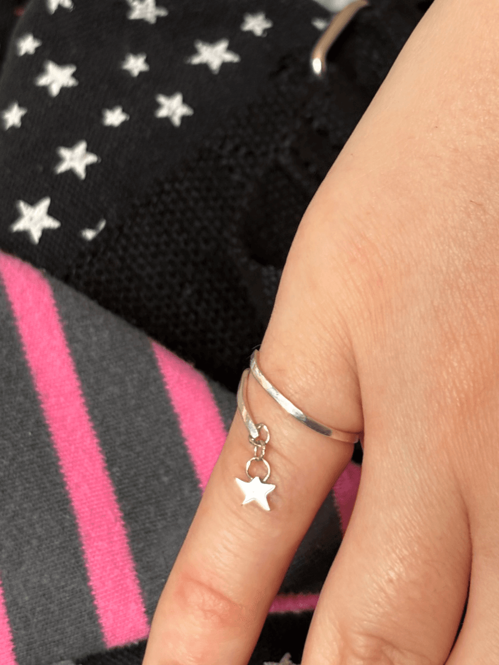 Vue rapprochée d'une bague ouverte argentée portée sur la main avec son pendentif étoile pendant.